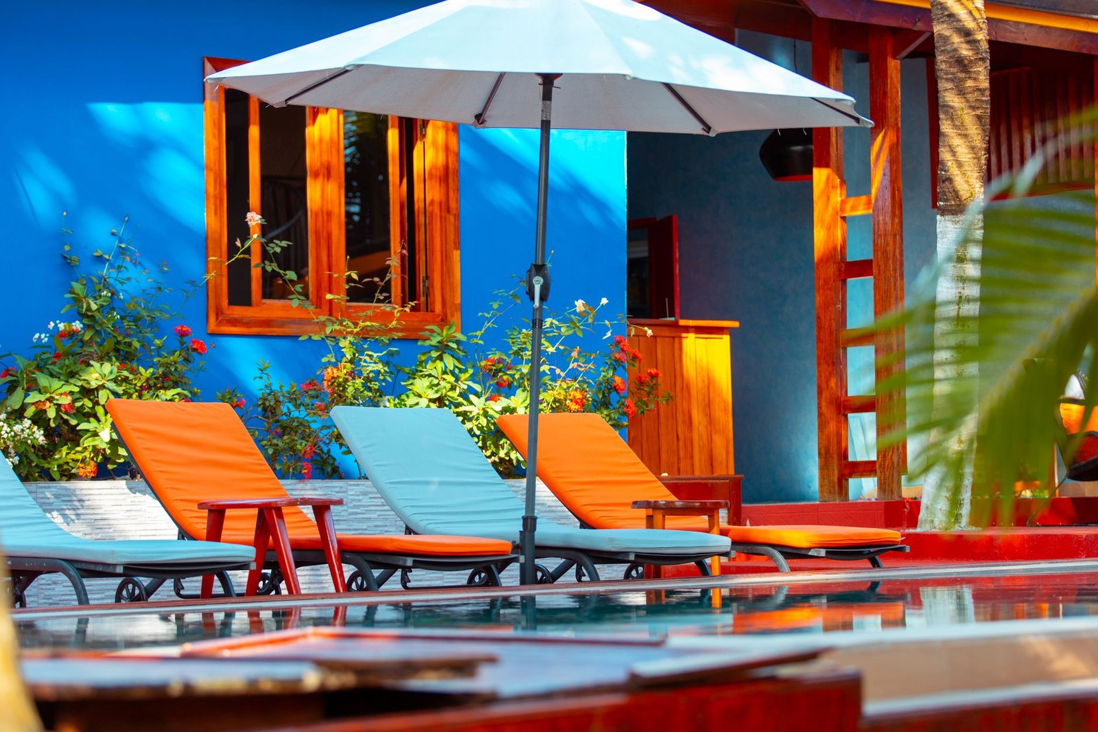 Bains de soleil en résine tressée au bord d'une piscine d'hôtel, avec coussins et parasol