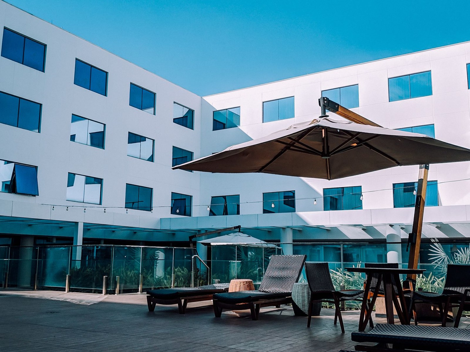 Terrasse d'hôtel équipée de bains de soleil en résine tressée et d'un parasol déporté, prête avant l'ouverture de la saison