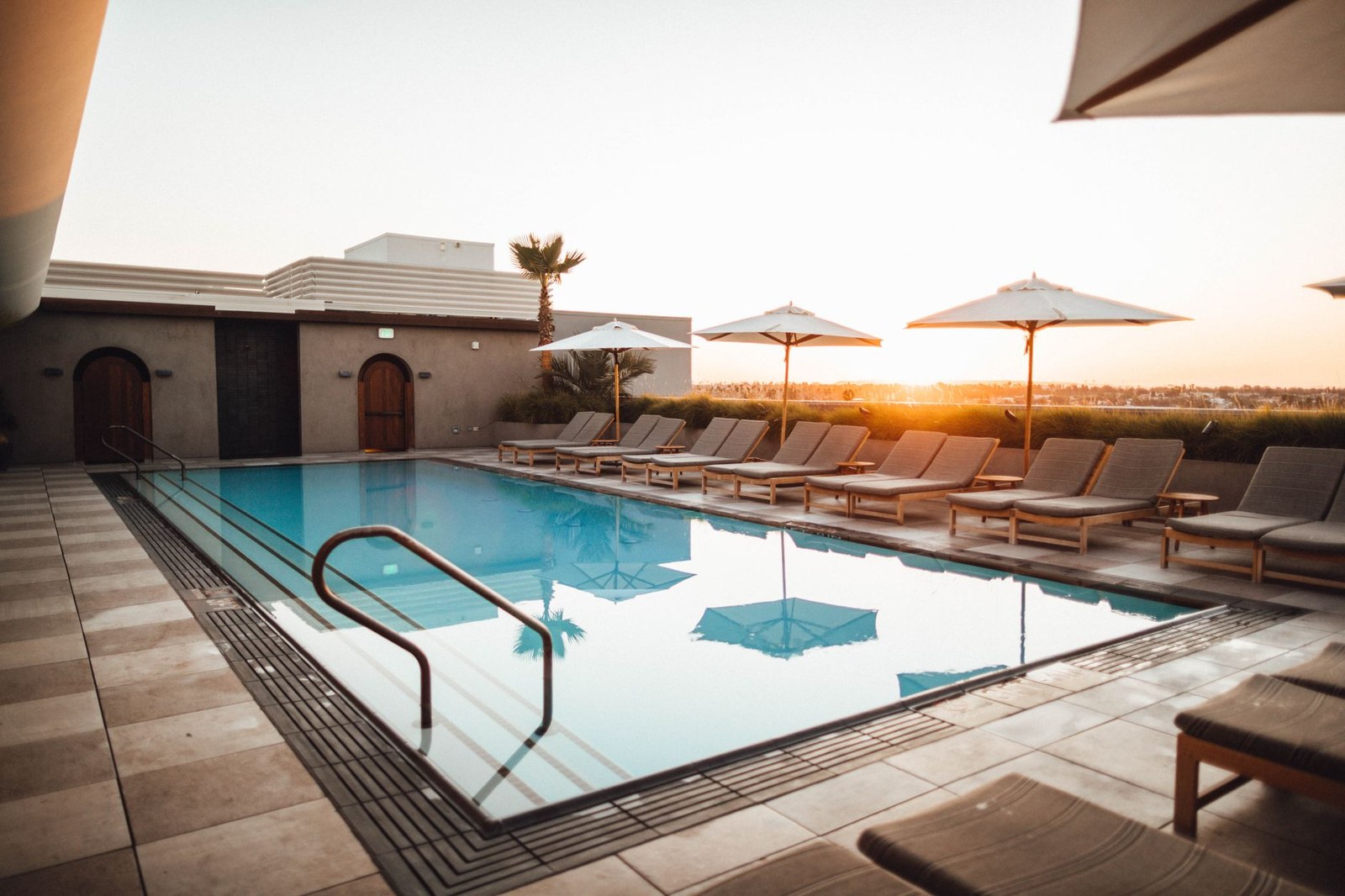 Terraza de piscina de hotel con tumbonas de madera, mesas auxiliares y sombrillas blancas al atardecer, mobiliario exterior de fábrica china
