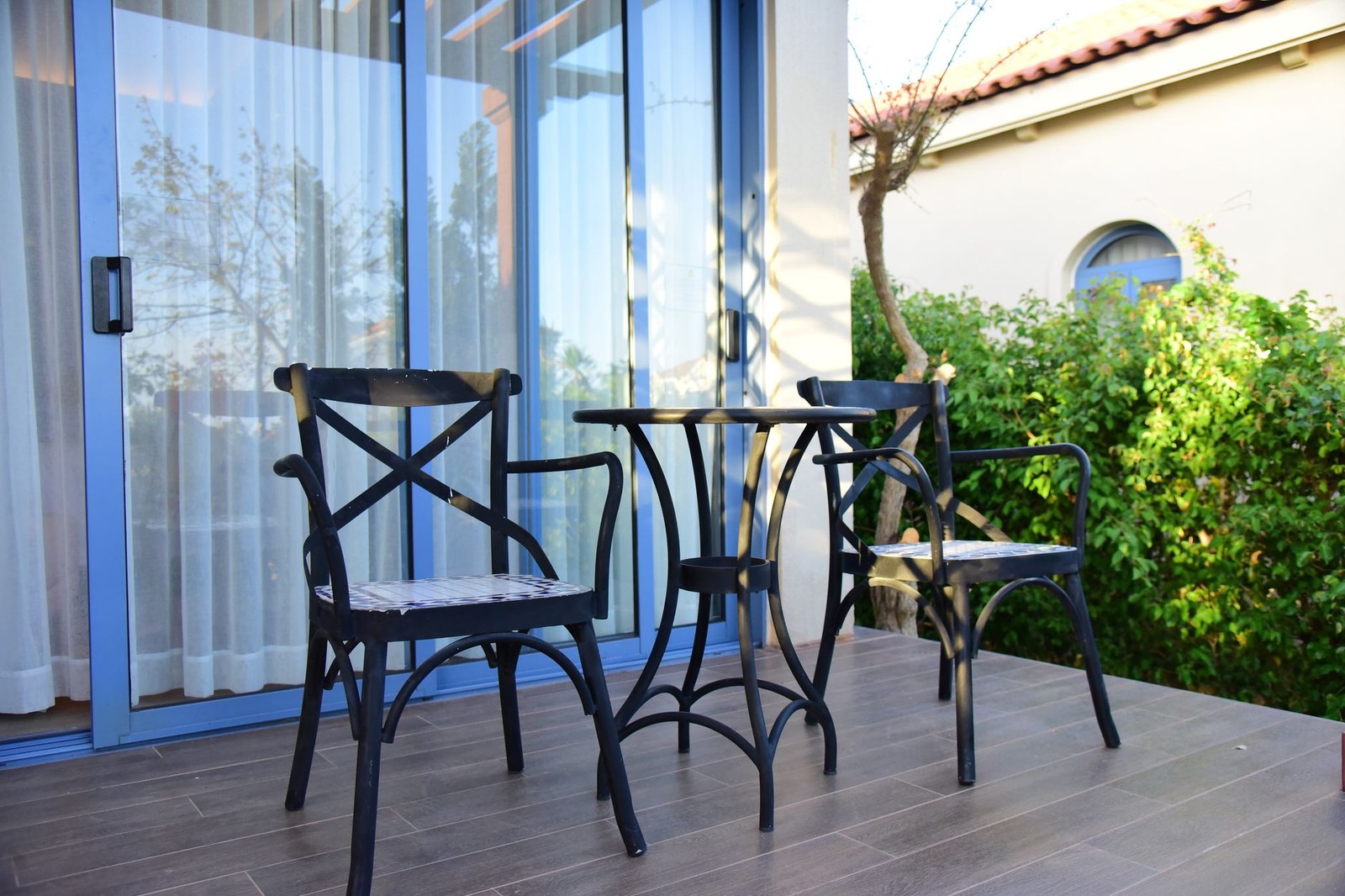 Conjunto de mesa y dos sillones de exterior en una terraza de madera junto a un jardín